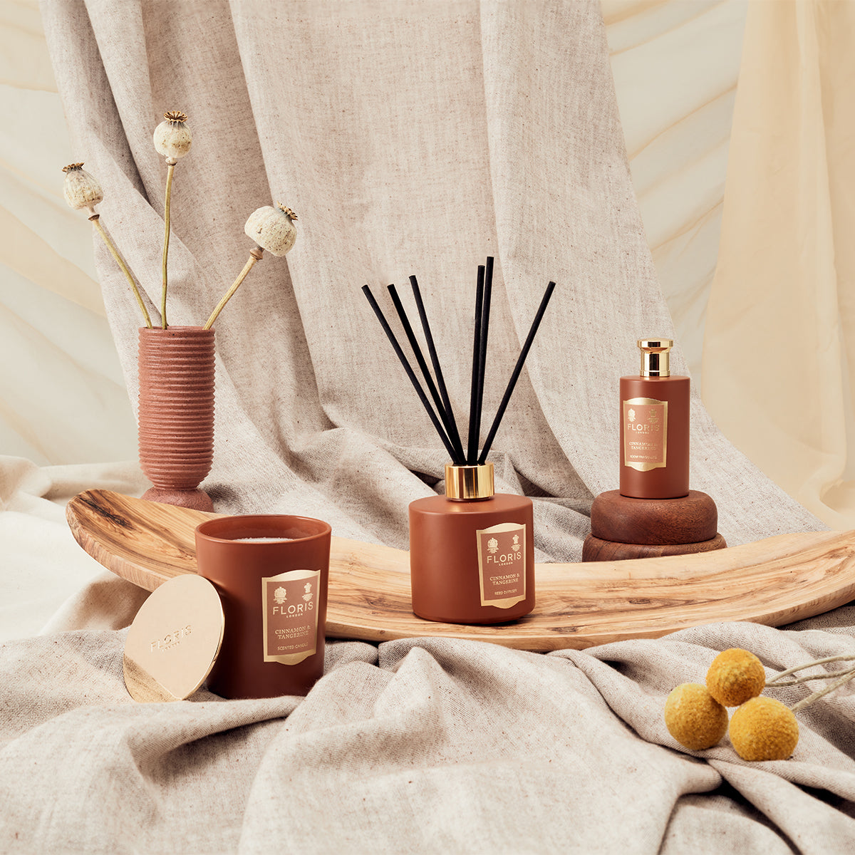 The Floris London Cinnamon & Tangerine Reed Diffuser 200ml brings a cozy fragrance vibe, styled with black reeds and dried flowers on beige fabric.