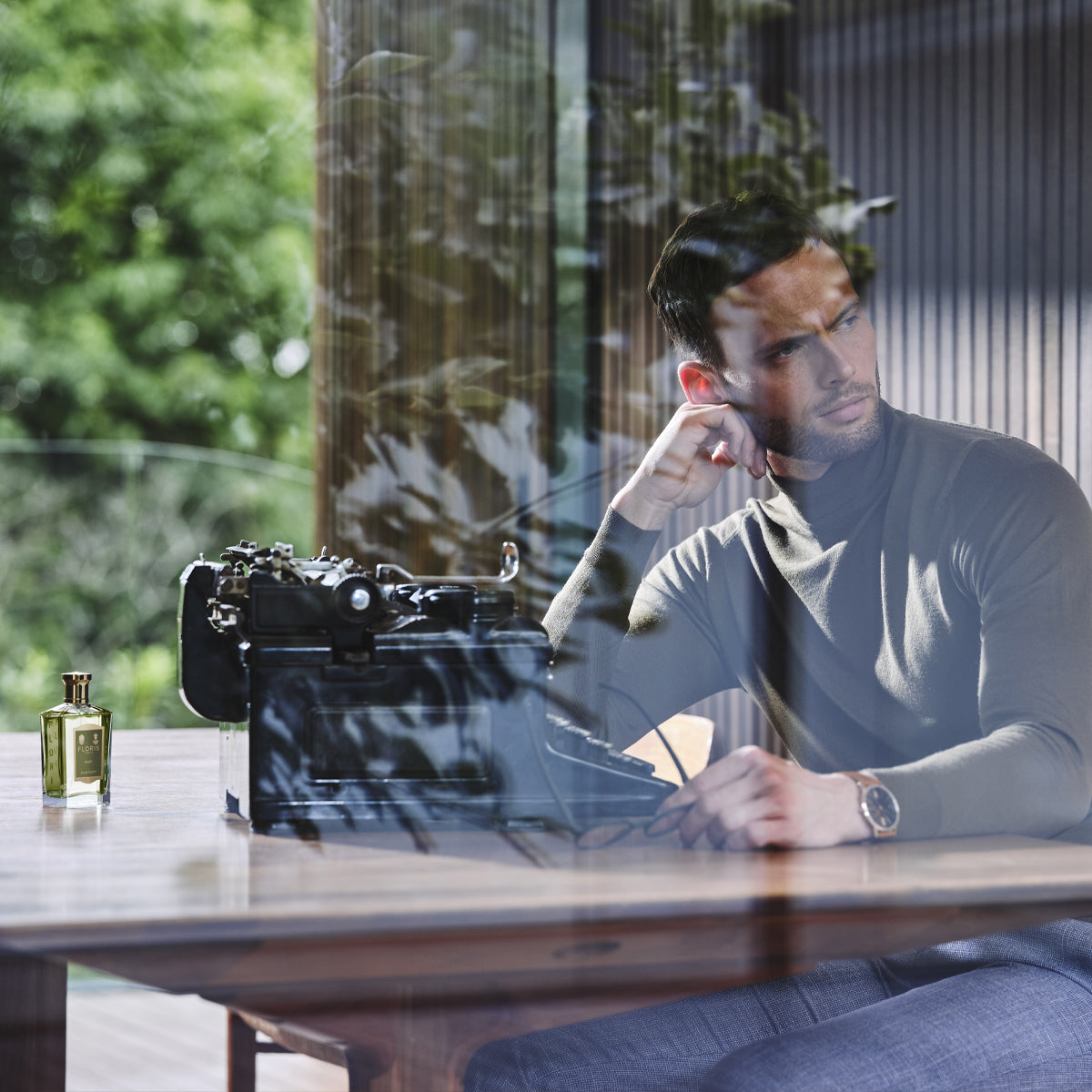 A man in a turtleneck sits by a typewriter, his skin glowing from rich hydration and antioxidant protection by Floris London Elite Facial Moisturiser.