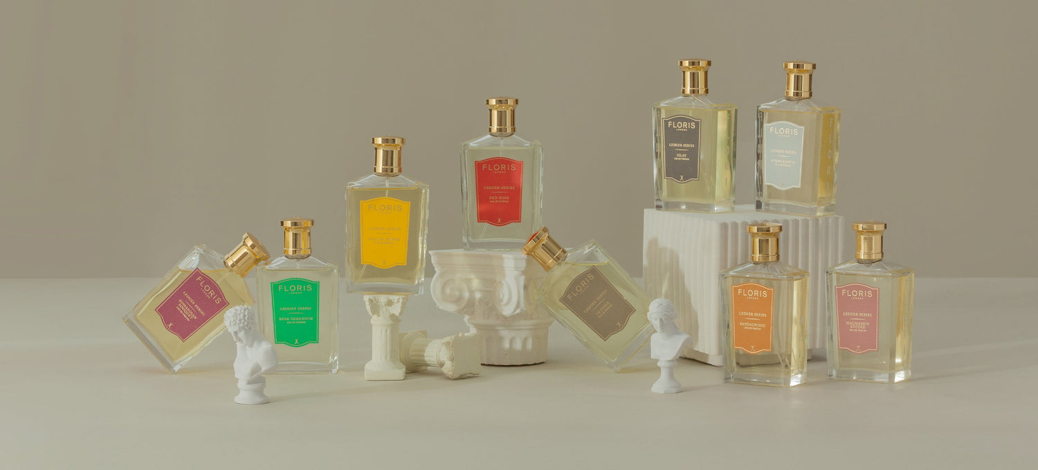 A collection of perfume bottles with gold caps displayed on white columns and busts against a neutral background.