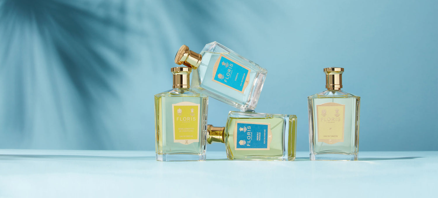 Four elegant perfume bottles with gold caps, labeled "FLORIS," against a blue background with palm tree shadows.