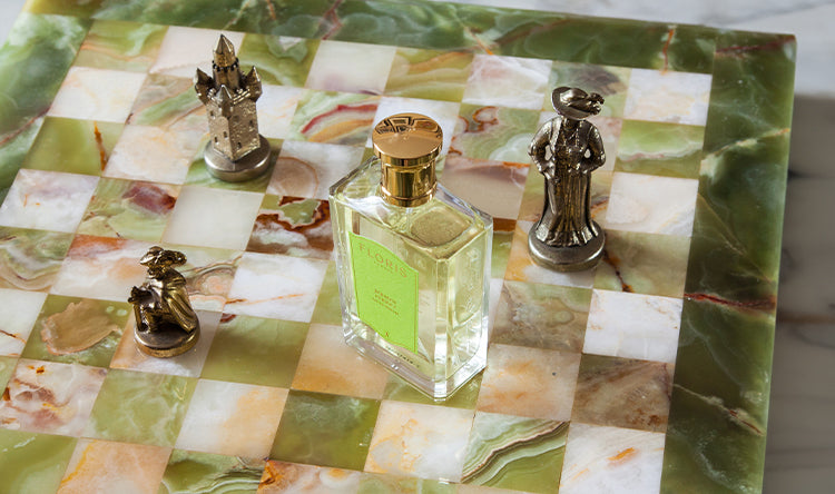 A glass bottle of perfume placed on a decorative chessboard with metal chess pieces.