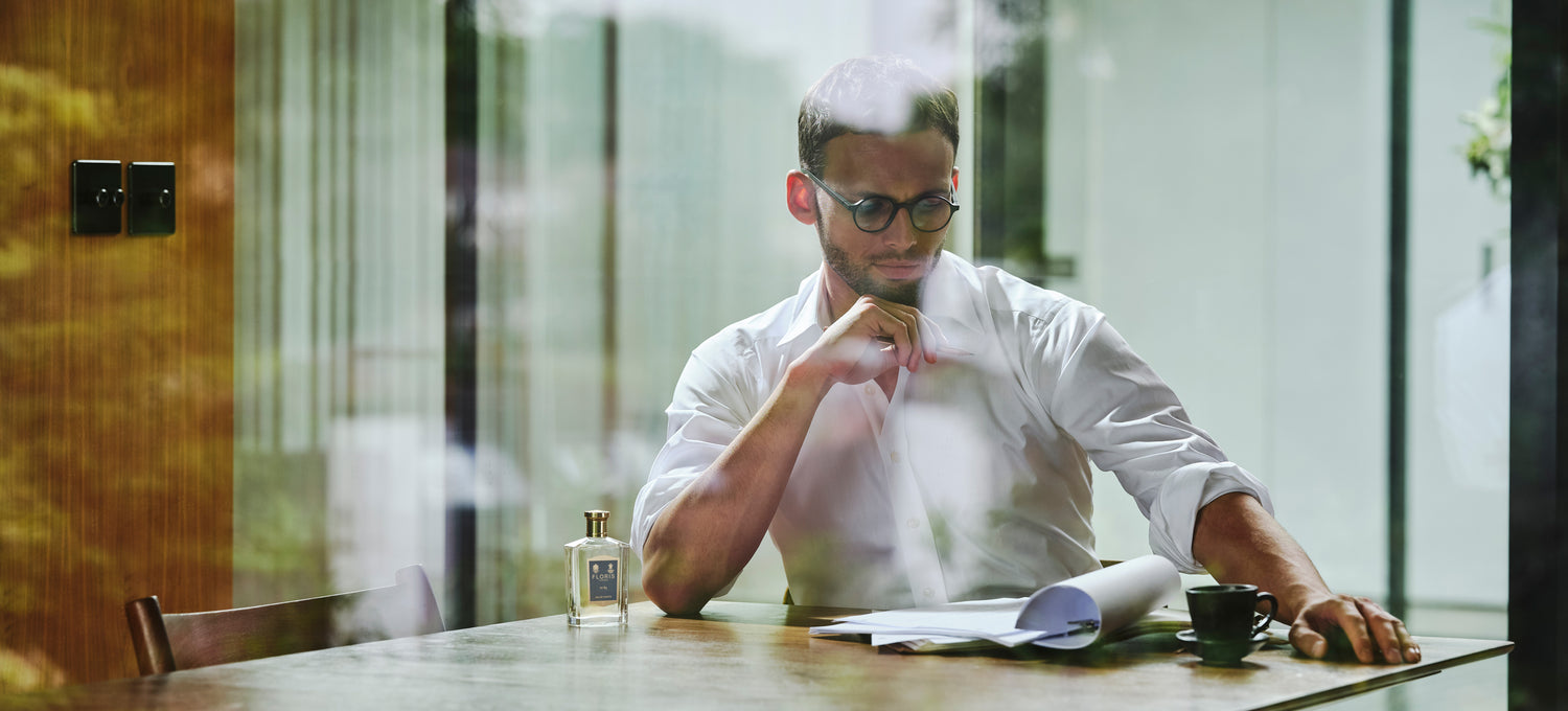 A man sitting and reading paperwork with a cup of coffee next to him and a bottle of No. 89.