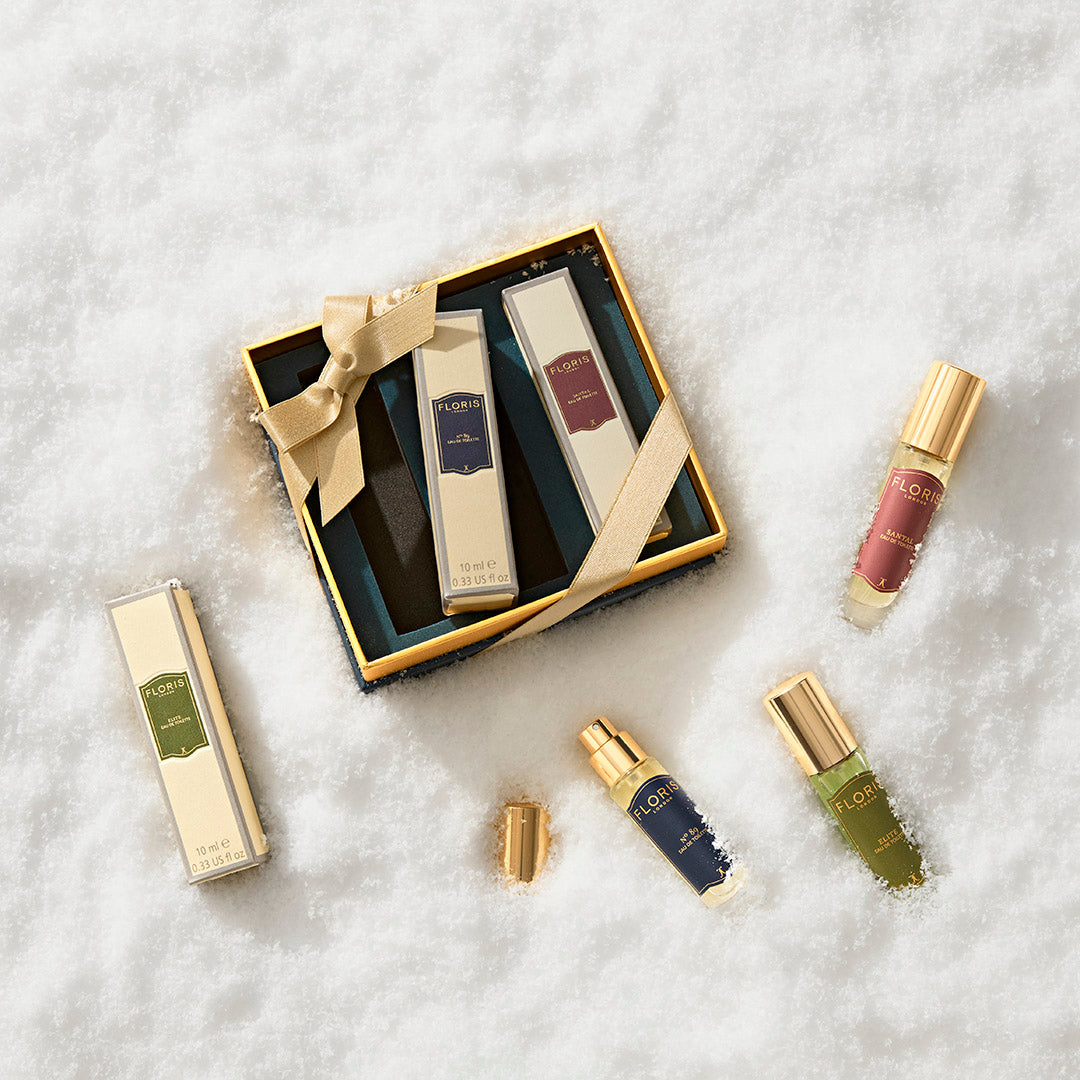 Floris London US Perfumer's Trilogy: For Him gift box with gold-capped perfume bottles on snow, one bottle open, ribbon tied on the box.