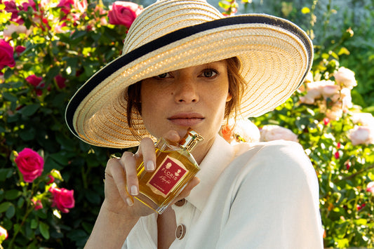 A Woman holding a bottle of Floris Londons A Rose For... in a sunlit garden filled with rose bushes