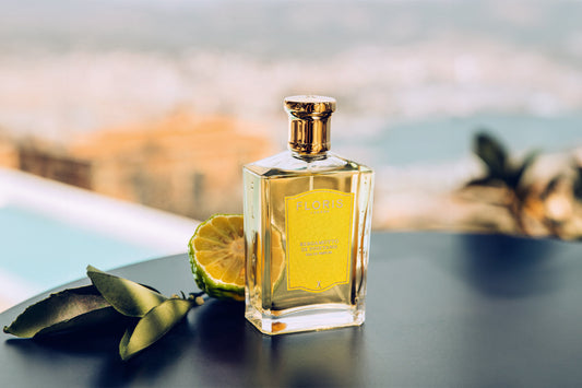 A bottle of Bergamotto di Positano on a table with a bergamot fruit, and a backdrop of italy. 