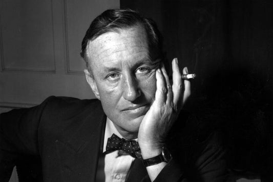 Black and white photo of Ian Fleming in a suit and smoking a cigar