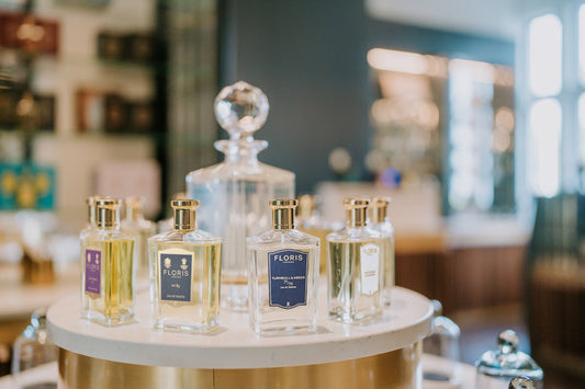 A display of Floris London fragrances showcased on a round marble stand, featuring elegant glass bottles with gold caps. Prominent labels include "No. 89" and "Turnbull & Asser 71/72," set against a luxurious boutique interior with soft lighting and blurr