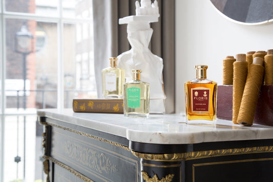 A bottle of White Rose, Rose Geranium and Leather Oud, on a ornate marble table  in front of a sunlit room.