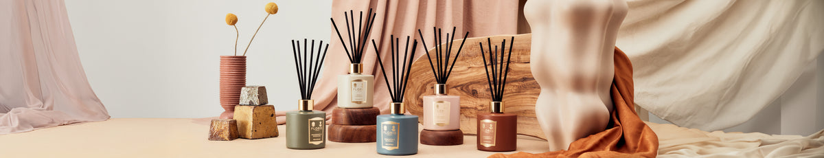 Aesthetic display of scented candles and reed diffusers with a nude art sculpture and draped fabric backdrop.