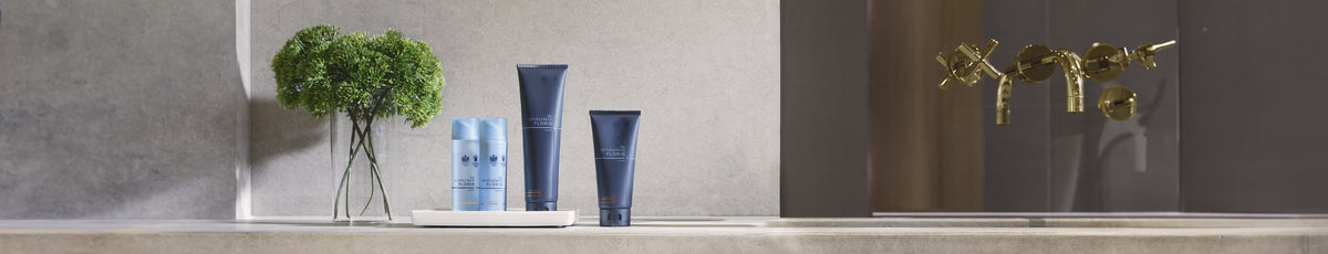 Skincare products on a bathroom counter with a plant and gold faucet.