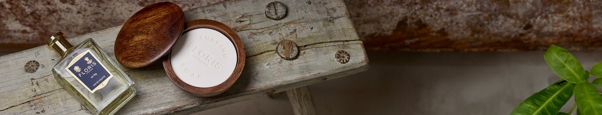 Perfume bottle and wooden soap container on a rustic wooden bench, with a green plant in the corner.