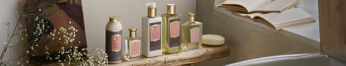 A collection of spa products on a wooden shelf beside an open book and delicate white flowers.