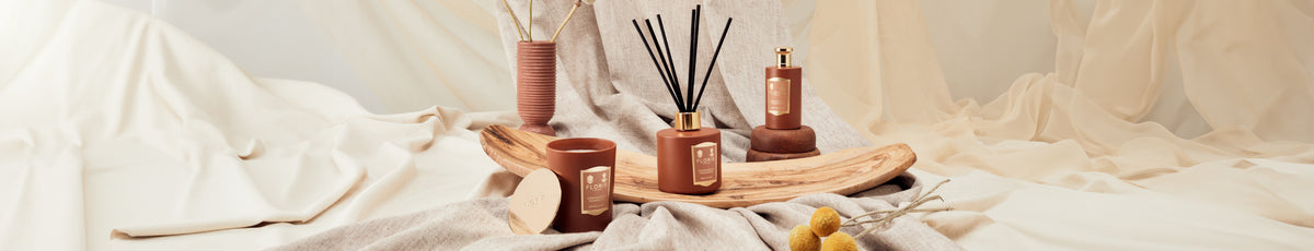 Aesthetic display of scented candles and diffusers on a wooden tray with draped fabric background.