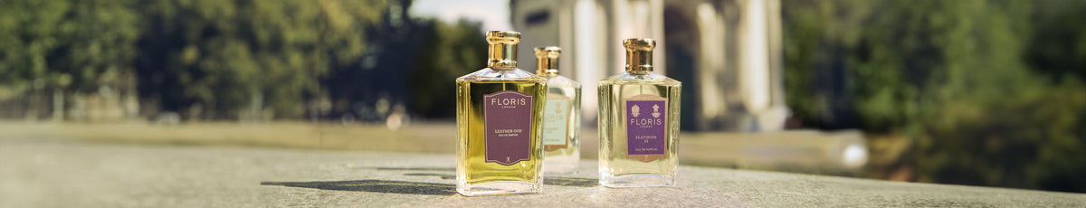 Three Floris perfume bottles on an outdoor ledge with blurred greenery and a structure in the background.