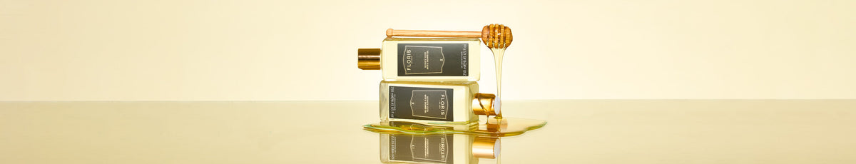 Two stacked glass jars of honey with a honey dipper, honey dripping onto a shiny surface.