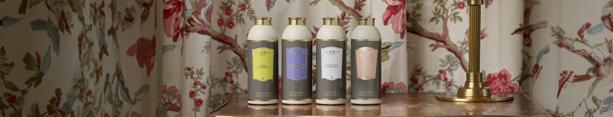Four floral-patterned lotion bottles on a vintage table with a floral wallpaper background.