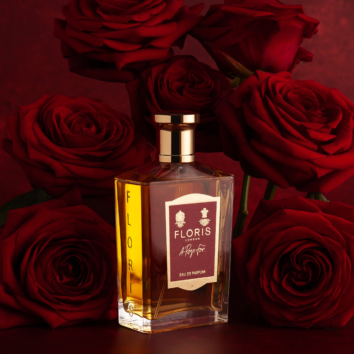 The "A Rose For..." Eau de Parfum by Floris London, surrounded by amber roses, exudes a rich fragrance against a dark red backdrop.