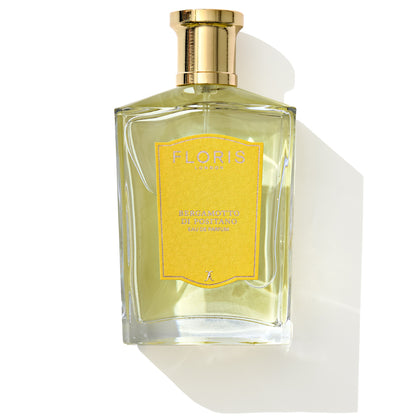 A glass bottle of Bergamotto di Positano Eau de Parfum by Floris London, adorned with a yellow label and gold cap, casts a shadow, capturing the essence of a fresh bergamot unisex scent inspired by the Mediterranean.