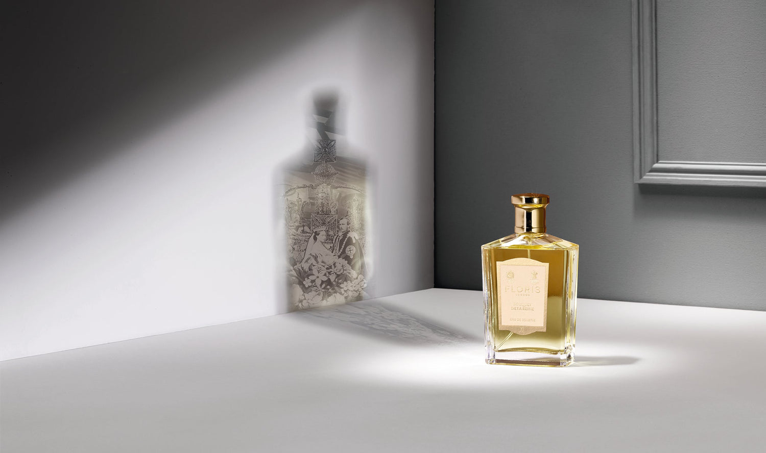 A gold-capped perfume bottle casts a shadow on a wall, revealing an intricate design not visible on the bottle itself.