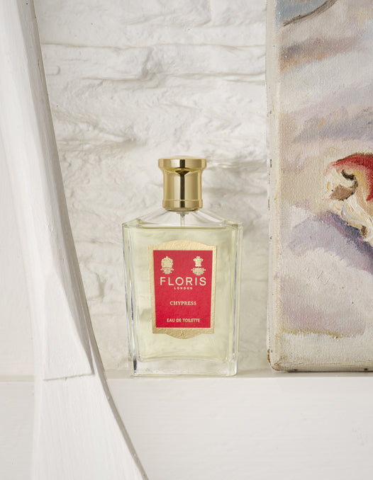 A Bottle of Floris London Chypress Eau de Toilette, placed upon a white wooden ledge, against a painted brick wall.