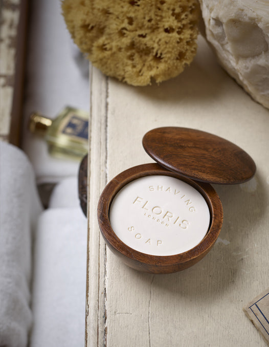 A Floris London No. 89 shaving bowl and soap set placed beside a bathroom sink, accompanied by a natural sea sponge, with a bottle of No. 89 Eau de Toilette visible in the background.