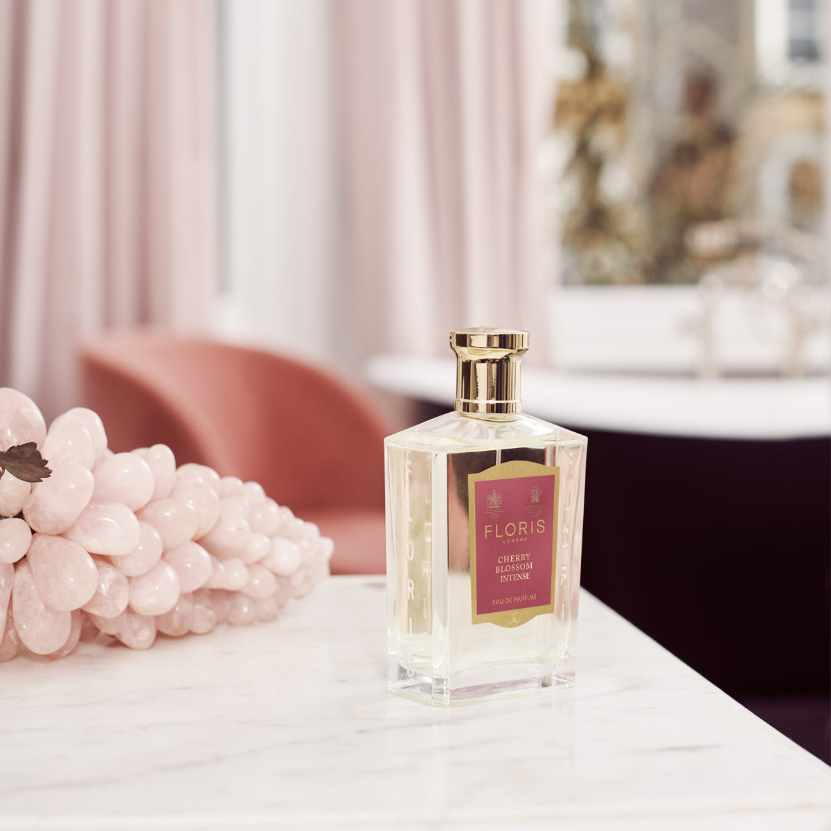 Perfume bottle on marble counter, pink sculpture, soft pink furnishings with a hint of Cherry Blossom Intense Eau de Parfum by Floris London.