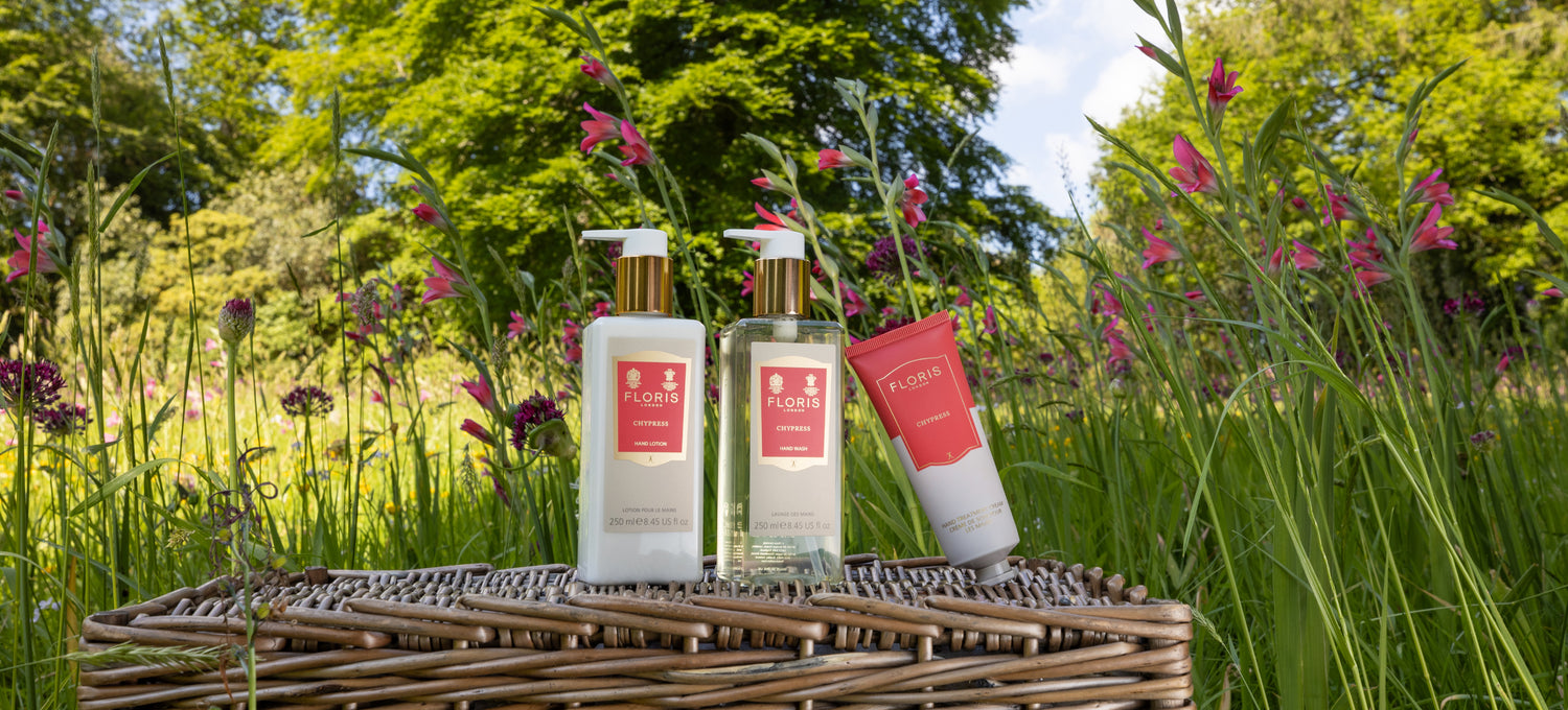 The Chypress hand collection resting on a picnic basket in a field adorned with pink flowers.