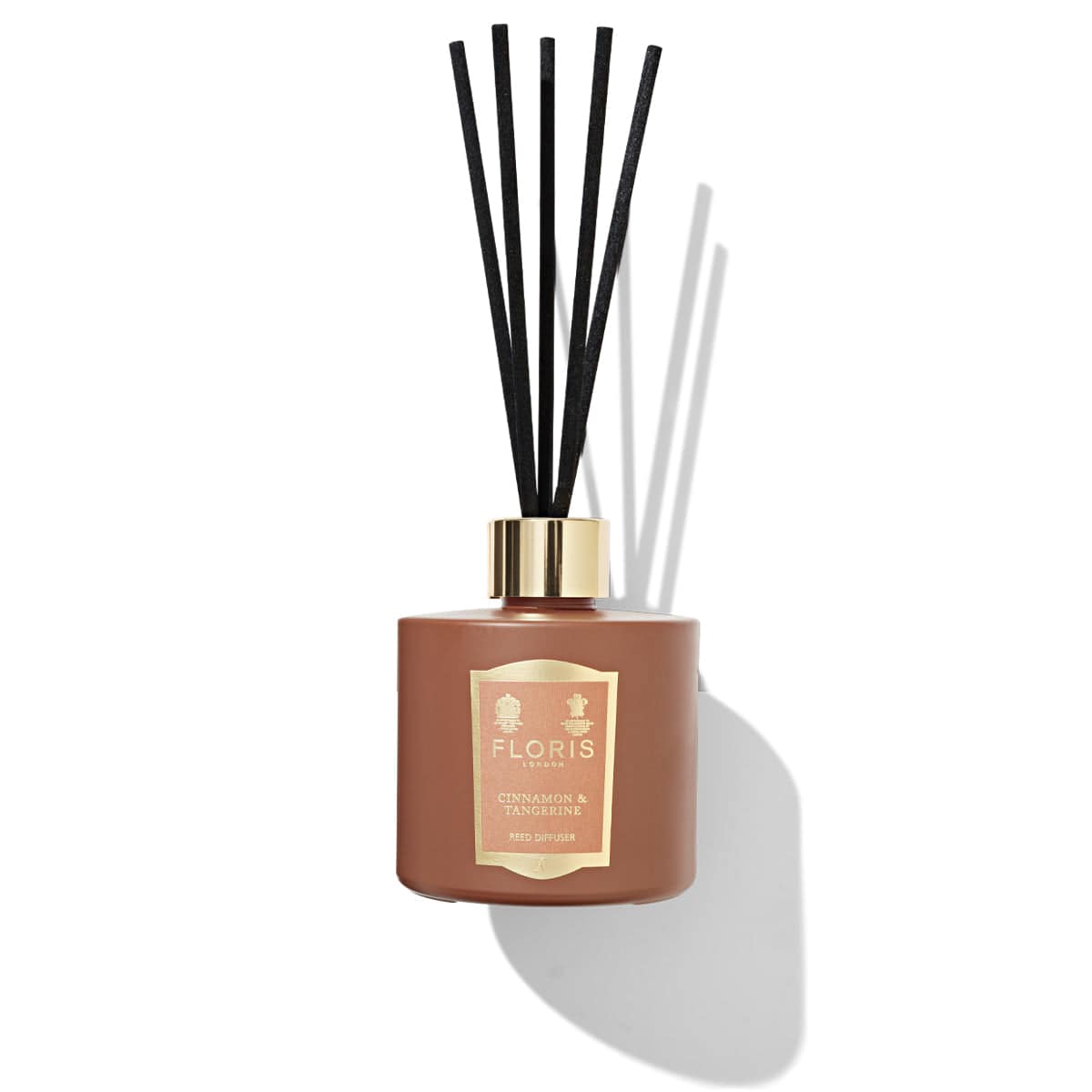 A Floris London Cinnamon & Tangerine Reed Diffuser bottle with black reeds, casting a shadow on a white background. The sleek glass vessel exudes an inviting aroma from its rich spice blend.