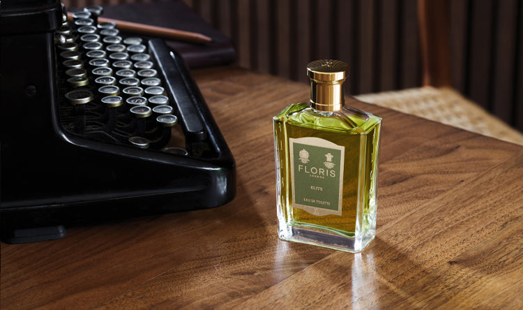 A bottle of Elite on a wooden desk next to an old-fashioned typewriter.