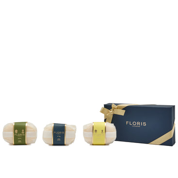 Three wrapped soaps with colored labels, including the delicate aroma of White Rose, are perfectly arranged next to a navy and gold Floris London "Soap Collection | For Him" gift box.