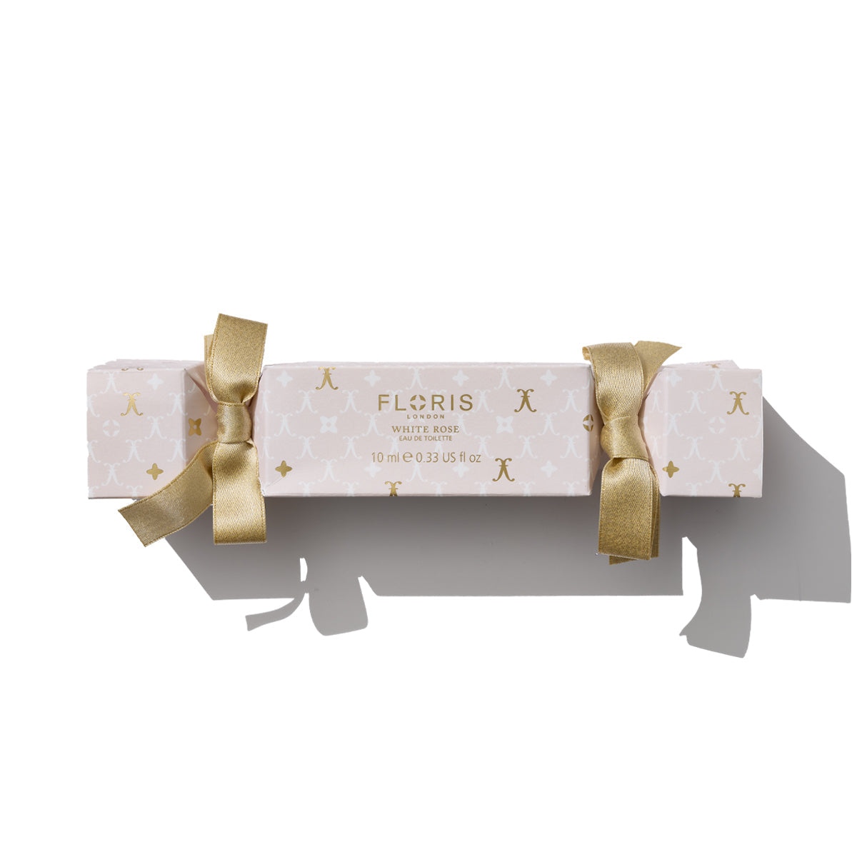 A cream and gold cracker-shaped box labeled "White Rose Holiday Cracker" by Floris London, adorned with gold ribbon bows on each end, evokes the charm of a holiday cracker—a delightful nod to British tradition during the holiday season.