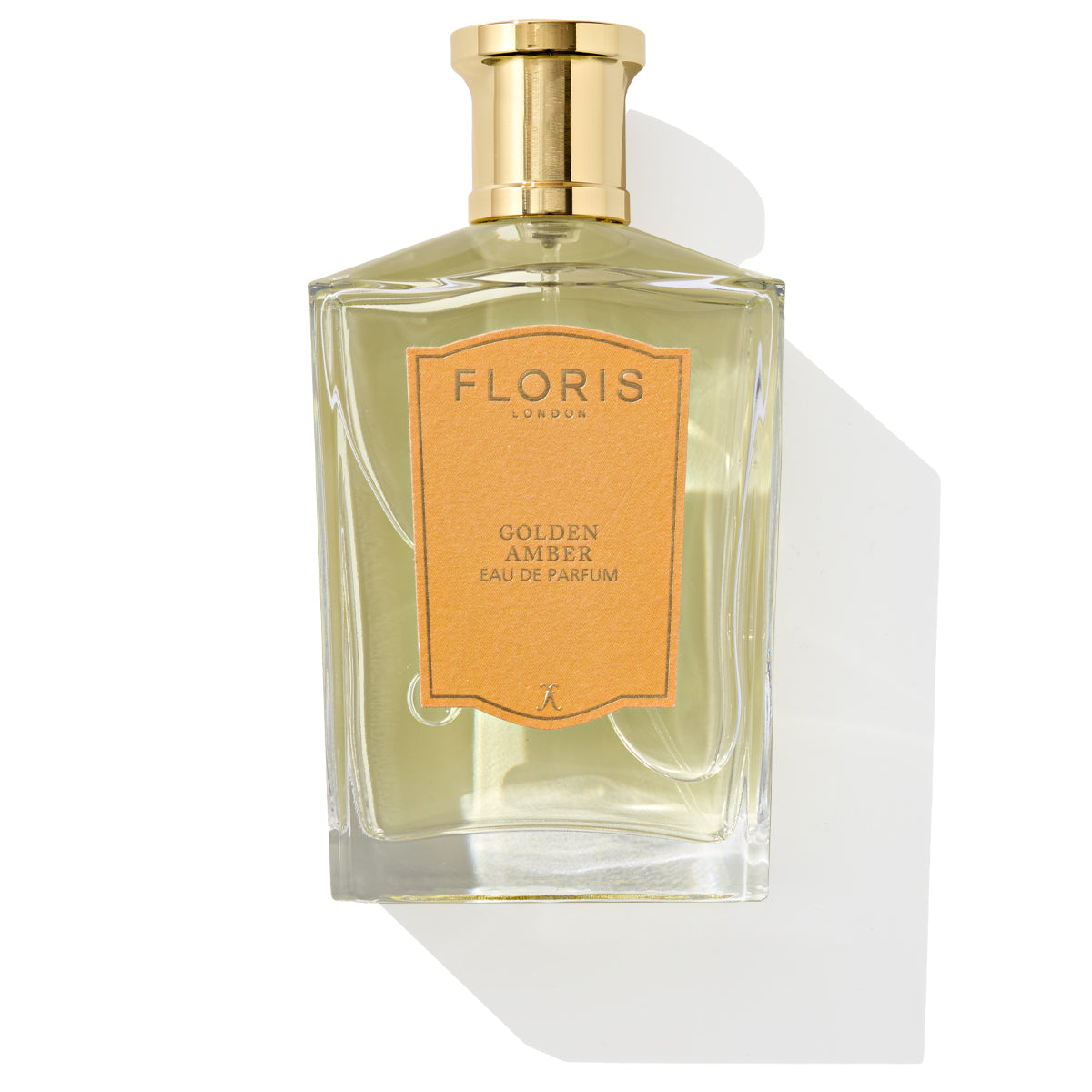 A bottle of Floris London's Golden Amber - Eau de Parfum, adorned with a gold cap and an orange label, casts a shadow as its floral heart mingles with subtle aquatic notes.