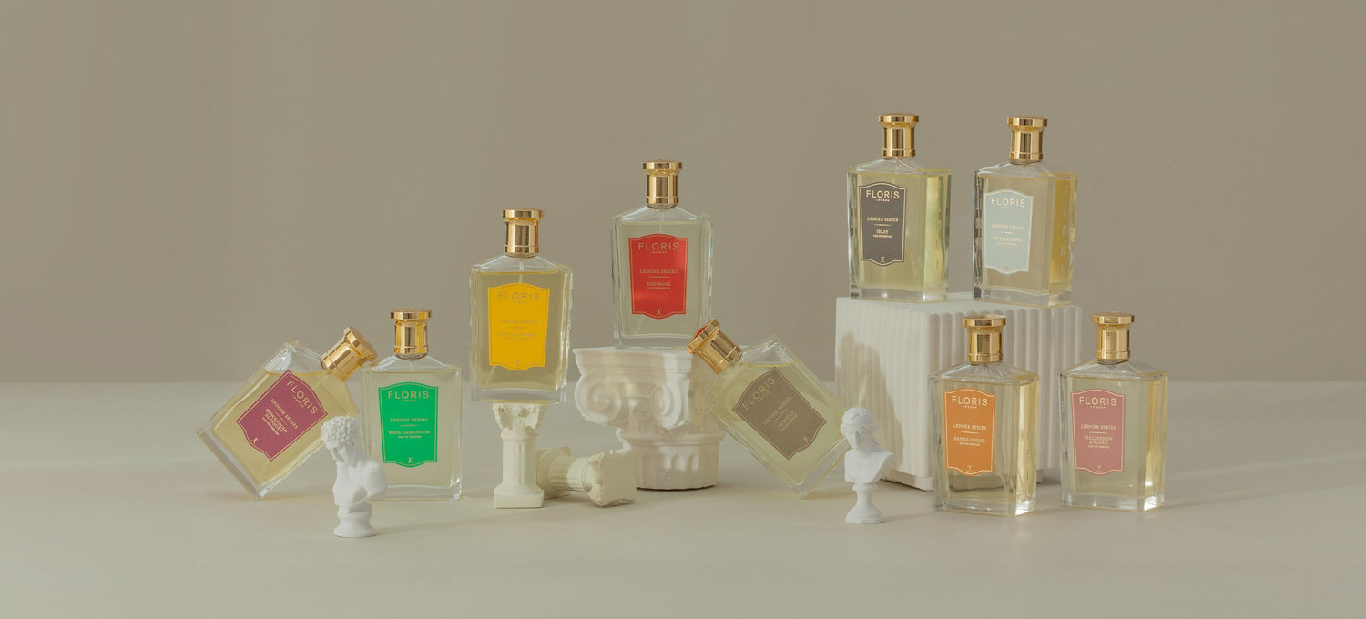 Various colorful bottles of perfume displayed with small white bust sculptures and columns on a beige background.