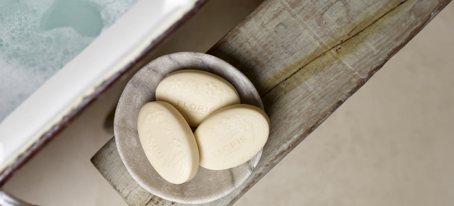 A collection of Floris soap, displayed in a marble stone bowl, next to a bath filled with water and suds. 