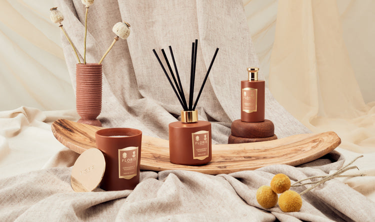 Aesthetic arrangement of a candle, reed diffuser, and spray bottle on fabric with wooden decor and dried flowers.