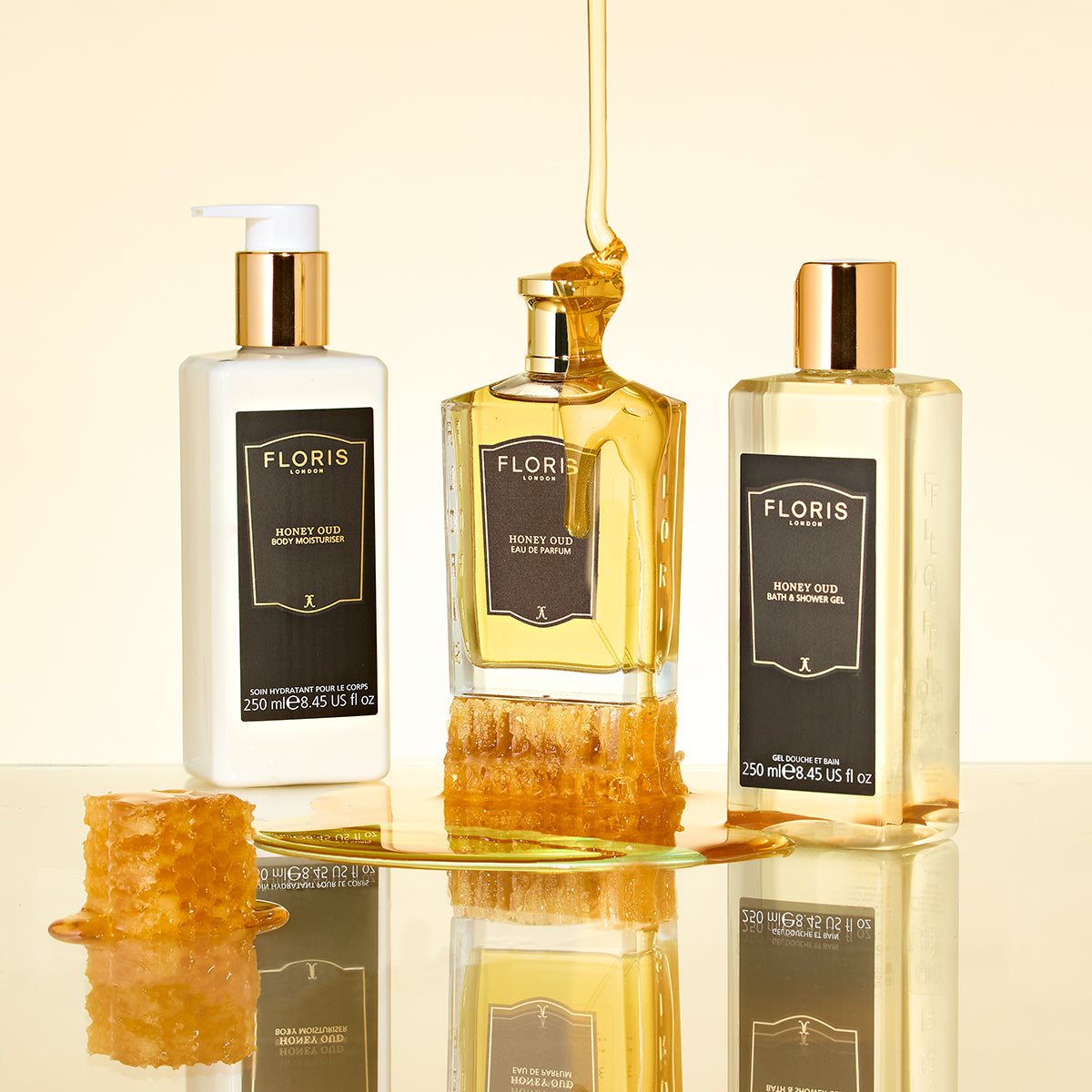 Three Floris London Honey Oud - Eau de Parfum bottles with English honey and honeycomb pieces on a reflective surface, golden background.