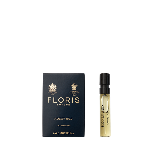 A Floris London Honey Oud - Eau de Parfum sample vial stands beside its navy blue and gold box, evoking the warmth of English honey and oud.