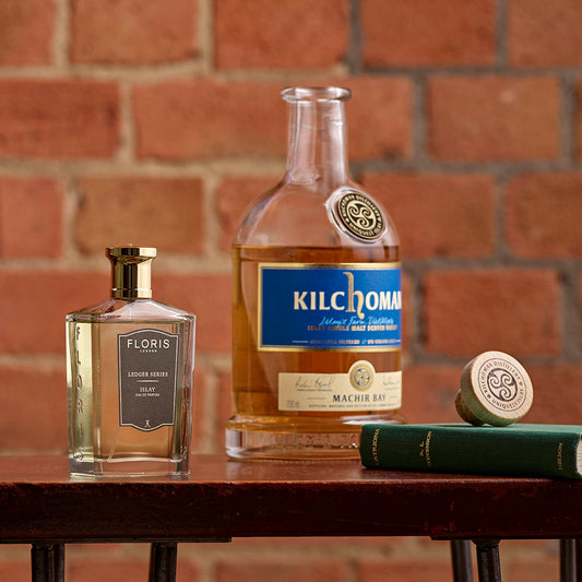 A bottle of Floris London Islay with bergamot notes and peaty, smoky whisky sits on wood against a brick wall background.