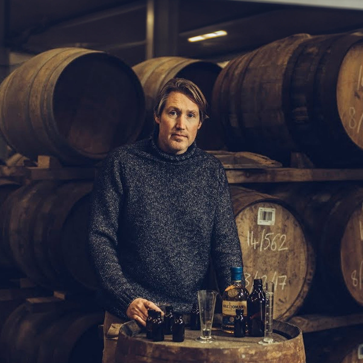 In a cellar, a sweater-clad person stands among barrels and bottles, savoring the peaty and smoky fragrance of Floris London's Islay whisky blends.