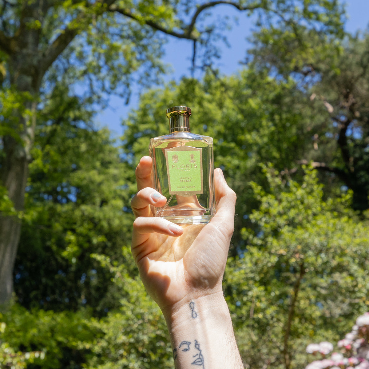 Hand holding a bottle of Floris London Jermyn Street - Eau de Parfum against green trees and blue sky, with exquisite vetiver notes.