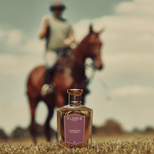 A Floris London Leather Oud Eau de Parfum bottle with a blurry rider in the background, outdoors. Captivatingly blends vetiver and oud oil.