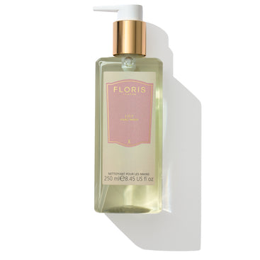 A bottle of Floris London Lily - Luxury Hand Wash, 250ml, featuring a gold pump dispenser and a pink label. Enjoy the uplifting floral fragrance that leaves a lingering trail on your skin.