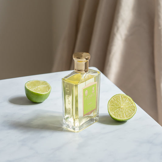 Floris London Limes Eau de Toilette with a gold cap sits on a marble table next to two lime halves.