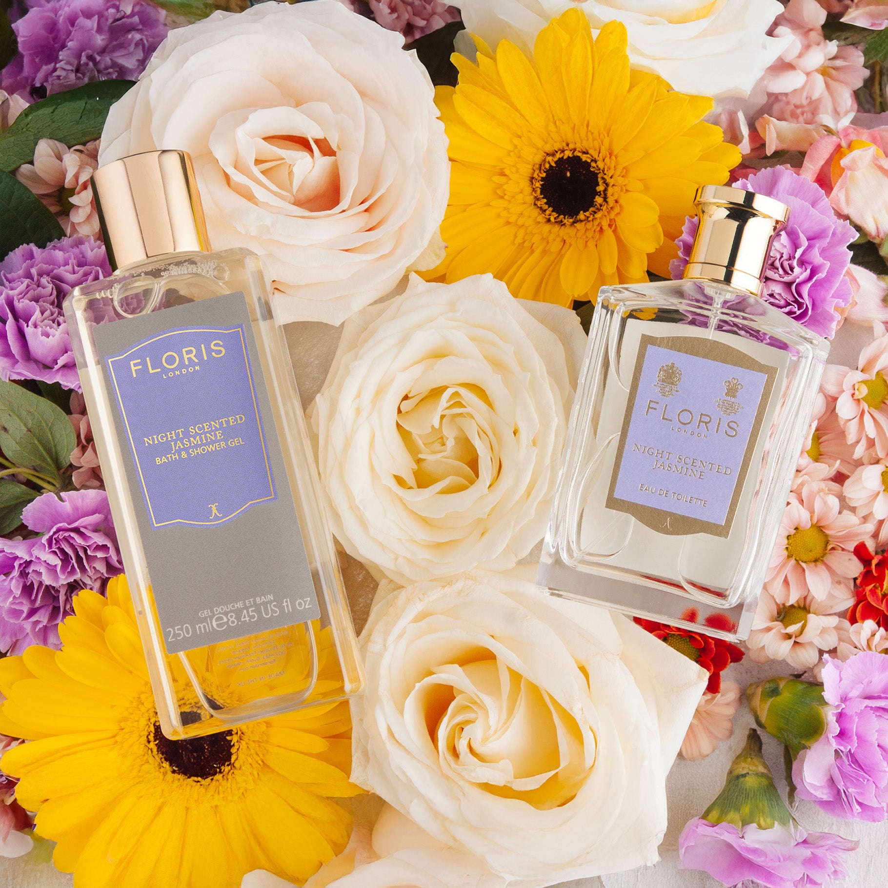 Floris London Night Scented Jasmine Mother's Day Pairing bottles surrounded by white roses, yellow gerberas, and pink and purple flowers.