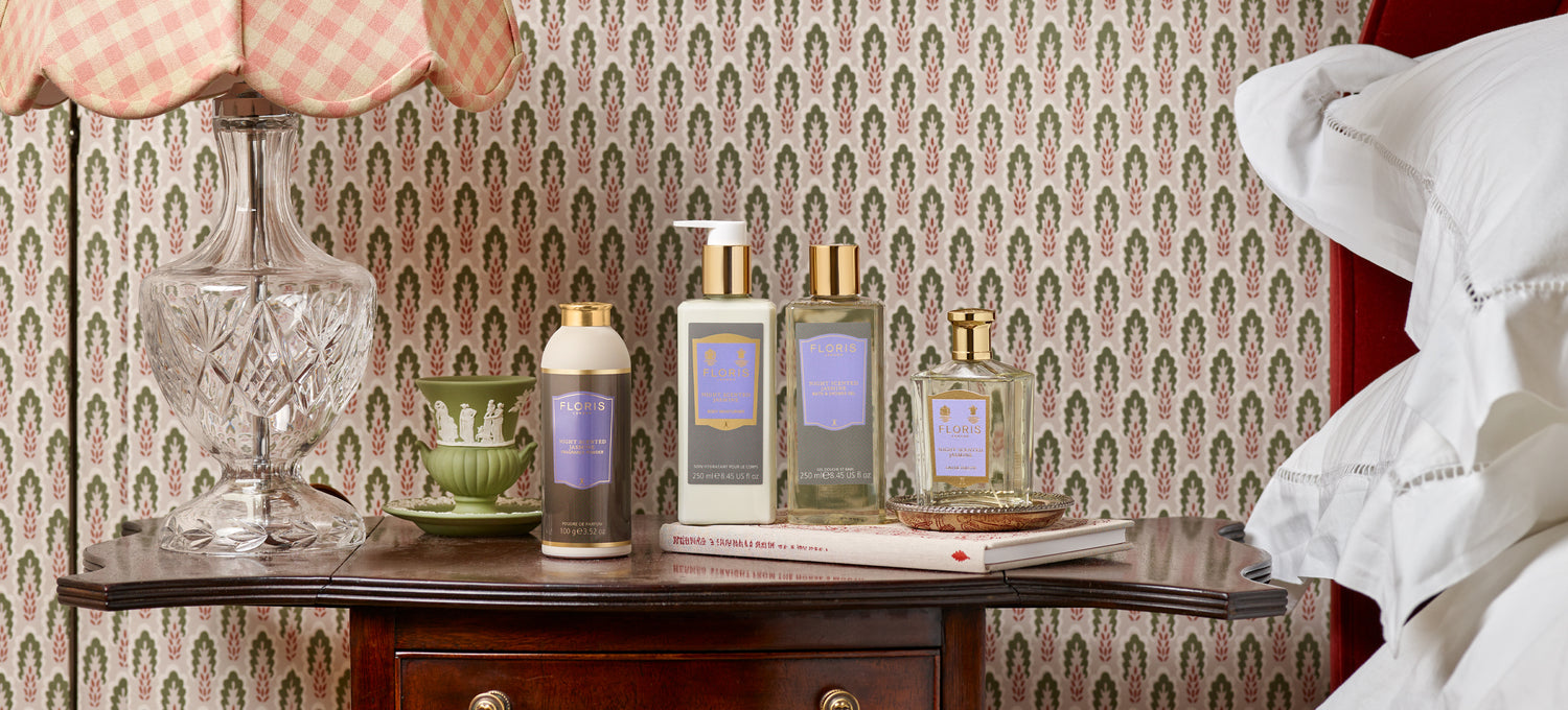 Night Scented Jasmine collection by Floris London US, displayed on a vintage bedside table with classic decor, including a crystal lamp and books, evoking a sense of elegance and comfort