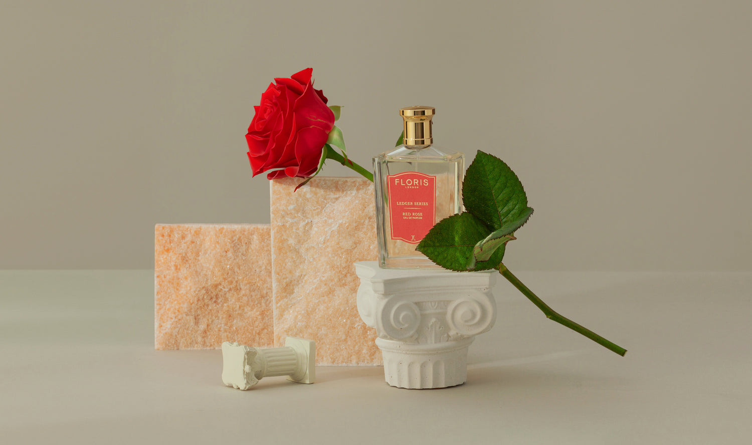 A bottle of Floris perfume next to a red rose on a sculpted pedestal, with stone tiles in the background.