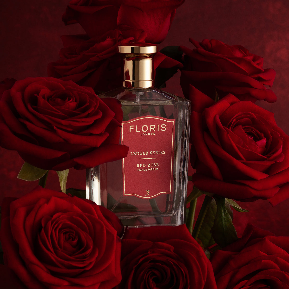 A "Floris London" Red Rose perfume bottle surrounded by fragrant red roses on a dark red background.