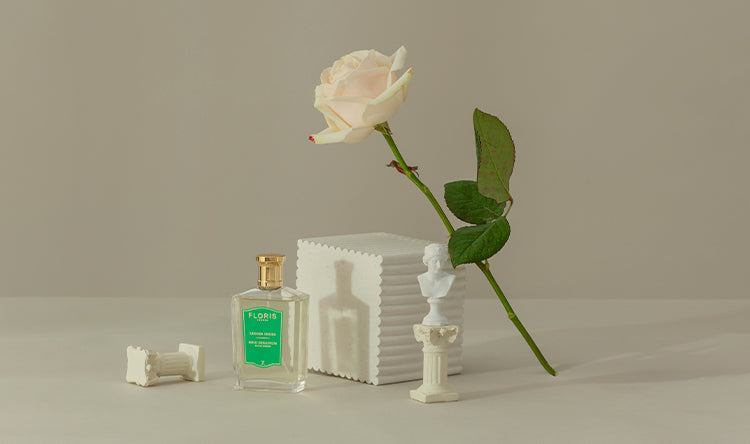 Perfume bottle, white rose, small statues, and marble decorations arranged against a minimalist beige background.