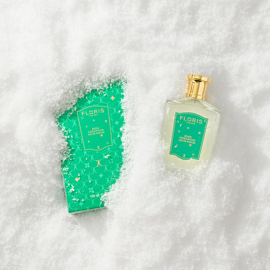 Floris London US Rose Geranium | Limited Edition perfume bottle and box, dusted with snow, rest side by side on a snowy surface.