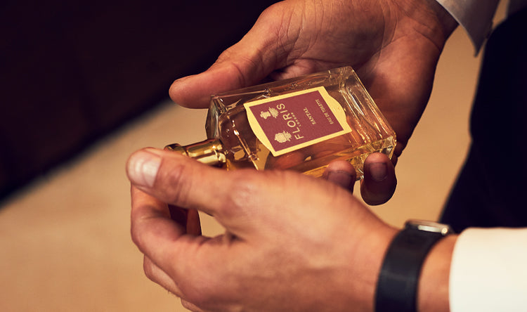 A man in a suit holding a bottle of Santal Aftershave by Floris London US, showcasing the exquisite craftsmanship and luxurious packaging of the product.